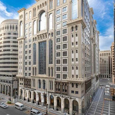 Al Aqeeq Madinah Hotel Medina Exteriör bild The photo depicts a large, modern building with a distinctive architectural style. The structure shows a blend of classic and contemporary design elements, featuring ornate details, large glass windows, and a prominent central facade. Surrounding the