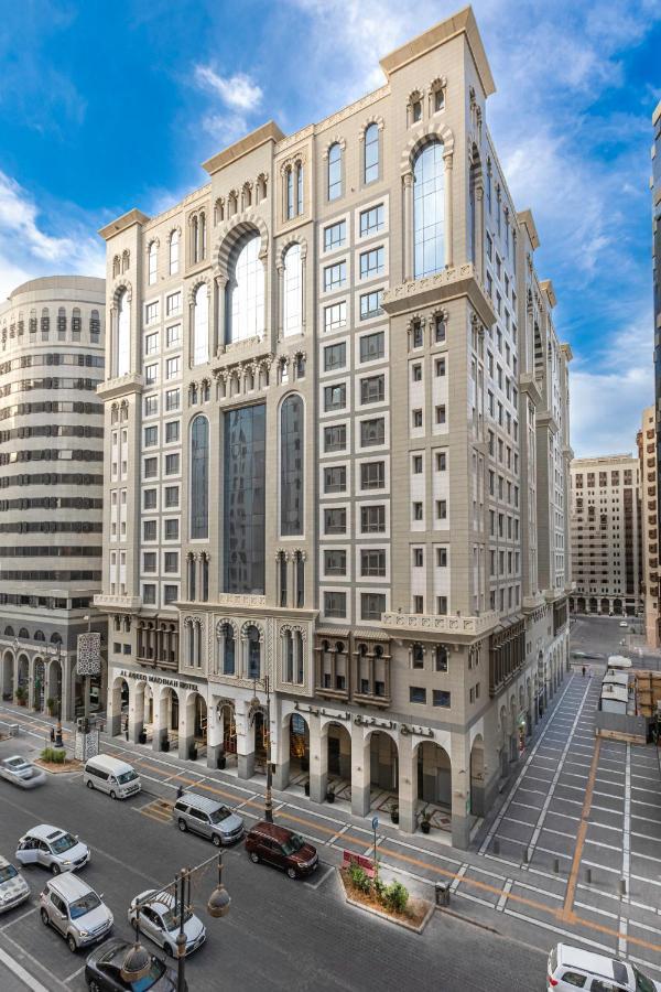 Al Aqeeq Madinah Hotel Medina Exteriör bild The photo depicts a large, modern building with a distinctive architectural style. The structure shows a blend of classic and contemporary design elements, featuring ornate details, large glass windows, and a prominent central facade. Surrounding the