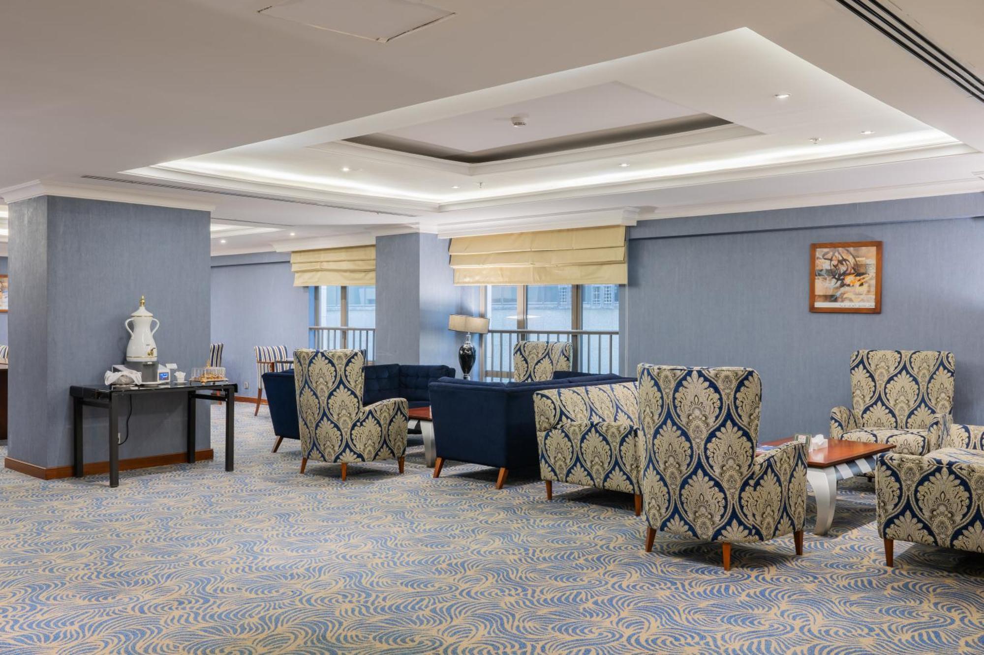 Al Aqeeq Madinah Hotel Medina Exteriör bild The photo shows a stylish indoor lounge or sitting area. It features several upholstered armchairs arranged around a central space. The chairs have a blue and cream patterned upholstery, creating a sophisticated ambiance. There is a table alongside s