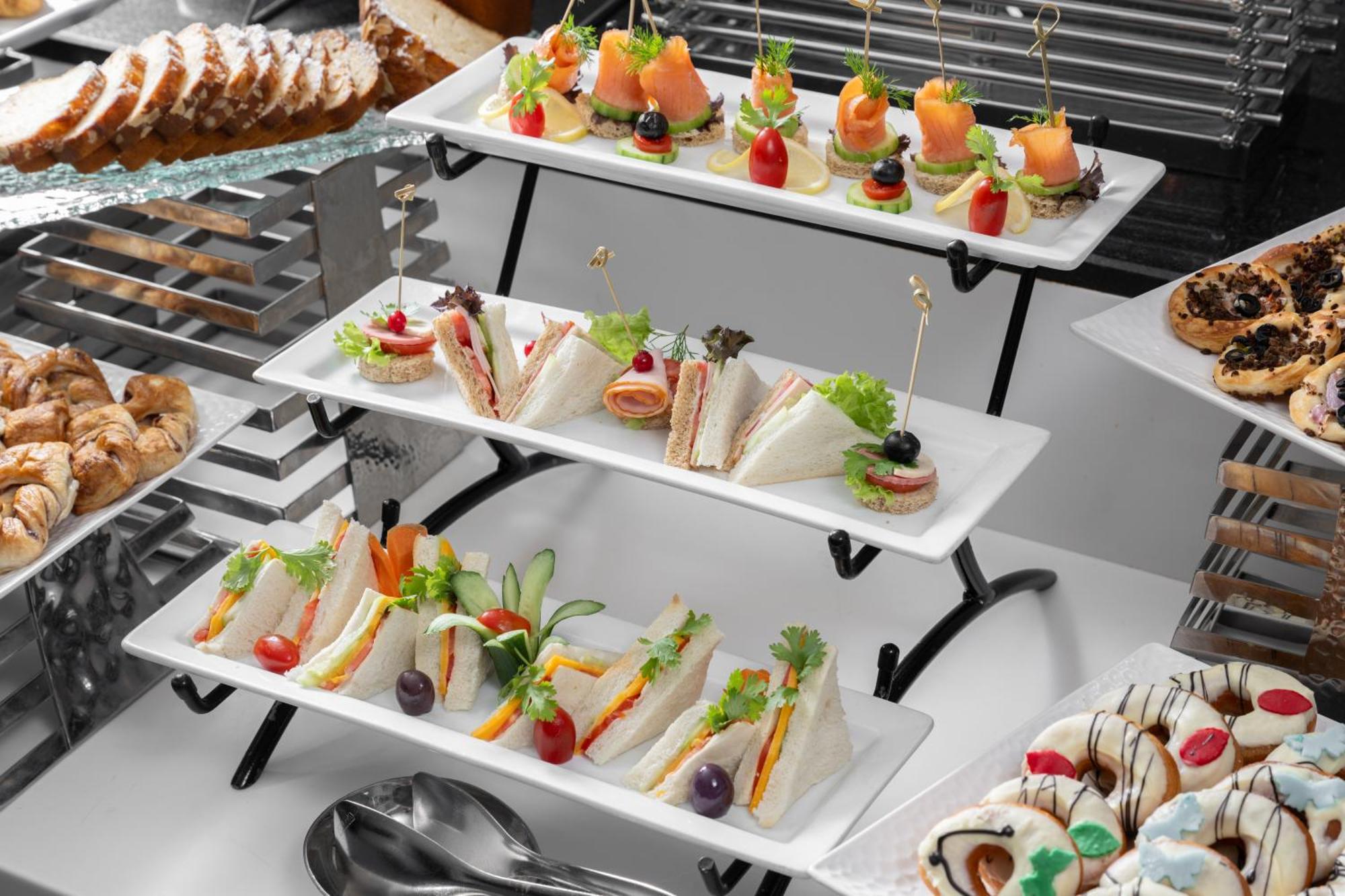 Al Aqeeq Madinah Hotel Medina Exteriör bild The photo shows a tiered display of assorted appetizers and snacks arranged on white rectangular plates. 

1. **Top Tier**: Contains small bites featuring smoked salmon garnished with greenery, and some with colorful cherry tomatoes on toothpicks. 

