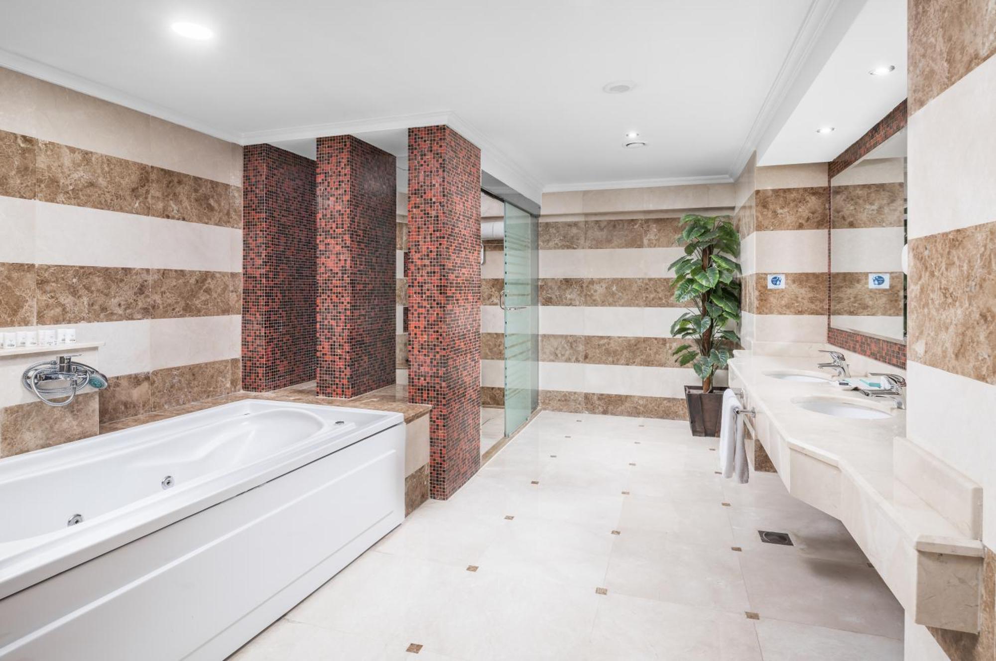 Al Aqeeq Madinah Hotel Medina Exteriör bild The photo shows a modern bathroom featuring a spacious layout. On one side, there is a large, white bathtub adjacent to a textured wall with warm, earthy tones. The walls are decorated with alternating horizontal stripes of light and dark colors. 

I