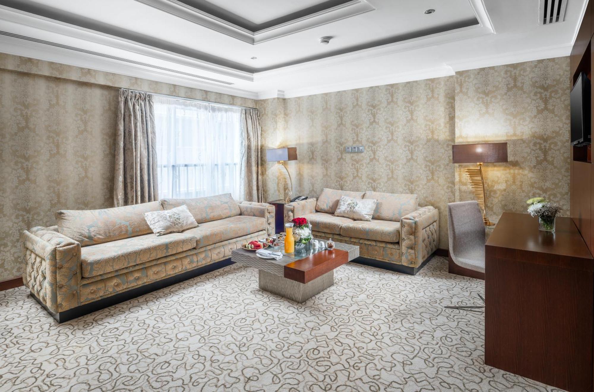 Al Aqeeq Madinah Hotel Medina Exteriör bild The photo shows a stylish living room with an elegant design. There are two beige sofas placed opposite each other, adorned with decorative pillows. A low coffee table is positioned in the center, featuring various items, possibly drinks or decorativ