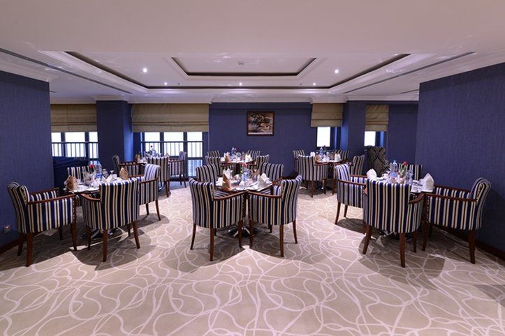 Al Aqeeq Madinah Hotel Medina Exteriör bild The photo shows an elegant dining room equipped with several tables. Each table is set with white tableware and neatly arranged silverware, giving a formal dining appearance. The decor features striped chairs and a carpet with a subtle pattern. The w