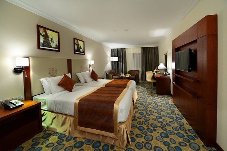 Al Aqeeq Madinah Hotel Medina Exteriör bild The photo shows a hotel room featuring two beds with white linens and brown throw blankets. There are decorative pillows on the beds. The room has a modern design, with wooden furniture including bedside tables and a large wooden unit that houses a t